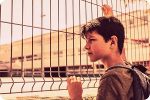 Autistic boy looking at school through a fence